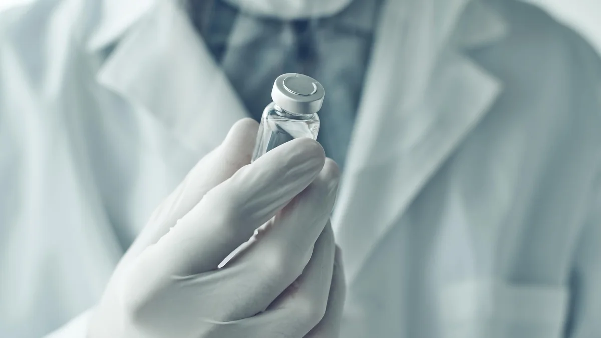 Gloved laboratory hands examining a small research vial.