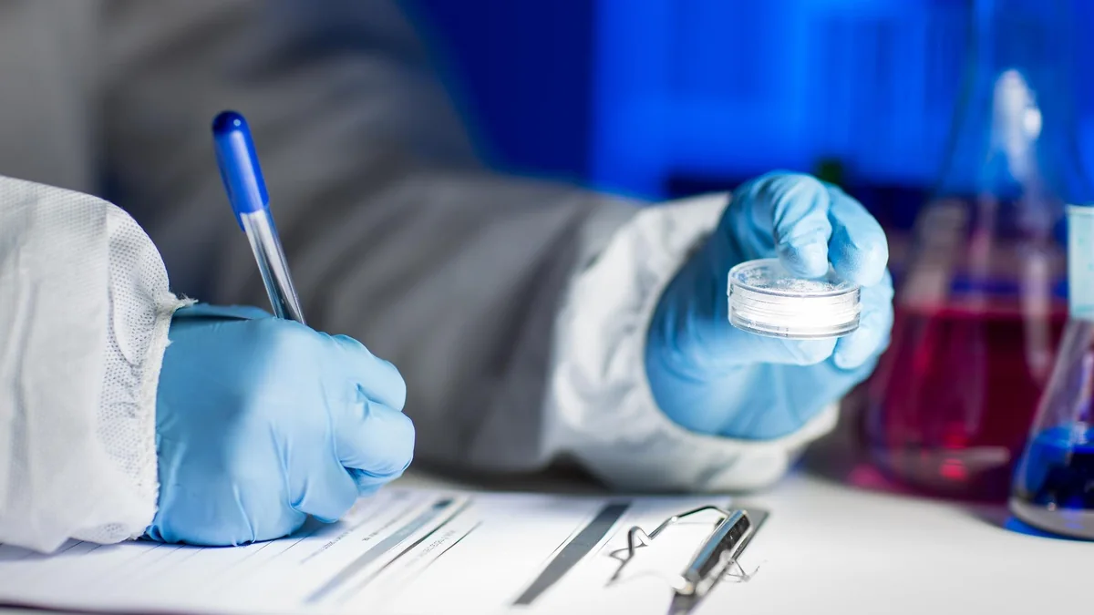 Gloved researcher recording observations beside a prepared laboratory sample.